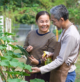 Two adults in a garden. Man looking at tablet screen held by woman.