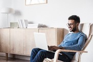 Man sitting in a chair looking at a laptop resting on his lap