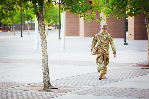 Uniformed man walking away while carrying books by his side