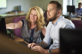 Woman instructor assisting male student at a computer station