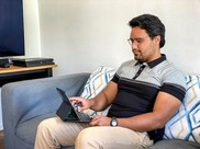 A man sitting on a couch while working on his tablet