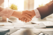 two professionals shaking hands over a desk with papers