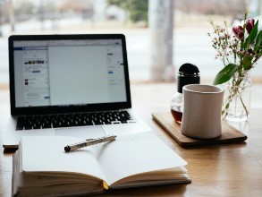 Laptop computer on a table with an open book in front of it and a mug next to the laptop
