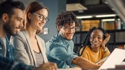 four students sit at table looking at a laptop