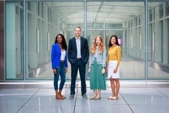 Four office workers viewed from a distance, standing in an office area