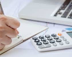 Hand writing in a journal, with a calculator nearby