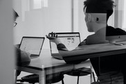 Black and white image of two students sitting together at a table with their laptops in front of them