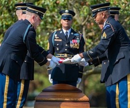 Service members place a flag over a casket