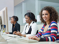 Three women working in a call center. Two are looking at their monitor. One is looking towards the camera