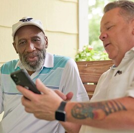 Two men use a smartphone to read about the Lifeline and Affordable Connectivity
