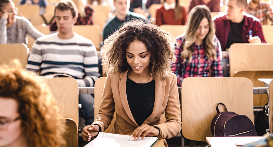 Woman looks down at her work while sitting in college classroom surrounded by other students