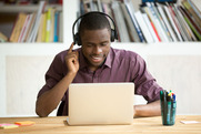 Man sits a table, working on his laptop while wearing headphones.