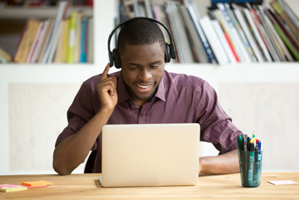 Man sits a table, working on his laptop while wearing headphones.