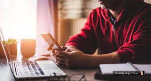 Person sitting at a desk in front of a laptop while looking at a cell phone