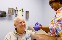 A VA nurse applies a small bandage to the shoulder of a smiling Veteran