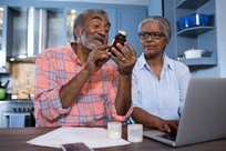 Man looking at medicine while sitting by woman using laptop