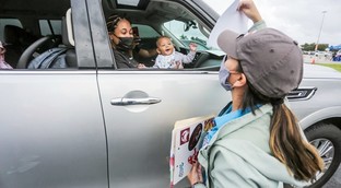 Woman passing giveaway to mother and child in car