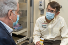 A male doctor talks with an older male patient. Both are wearing masks.