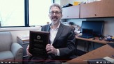Dr. Matthew Samore sits at his desk and holds an award he received
