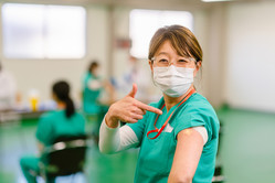 Masked health care worker smiling and pointing to bandaid after getting vaccine shot