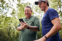 Two male Veterans as one receives and views a text on his cell phone.