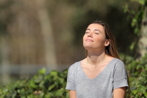 A smiling young woman with closed eyes lifts her face to the sun