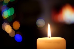 burning candle against a dark background with bright colored light behind