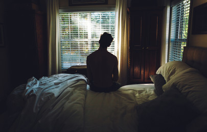 A man sitting on the edge of a bed in a darkened bedroom