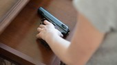 Amedium shot of a gun in a desk drawer and a womans hand pioking it up