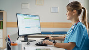 Precertificatiopn Woman in scrubs with stethescope around her neck enters information into a computer