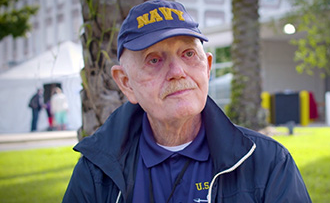 an older man outdoors wearing a cap that says "Navy"