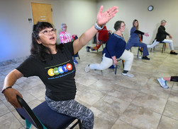Woman leading large yoga class sitting on chairs