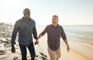 two smiling older men holding hands on the beach
