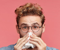 Young man with a tissue to his nose.