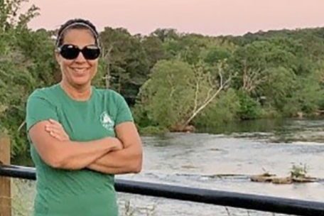 A smiling woman in a tee shirt standing in front of a river