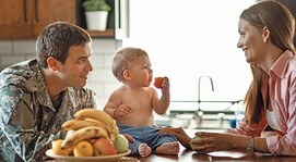 Baby sitting on a countertop between a man and woman smiling. 
