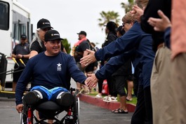 A disabled Veteran in wheelchair smiling while shaking people's hands. 