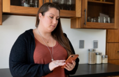 A person standing in a kitchen looks down at their phone.