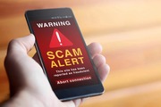 Hand holding mobile phone showing scam alert on the screen
