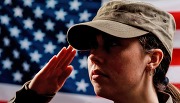 A woman in military uniform salutes in front of an American flag