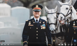 smiling soldier in dress uniform walking in front of two white horses