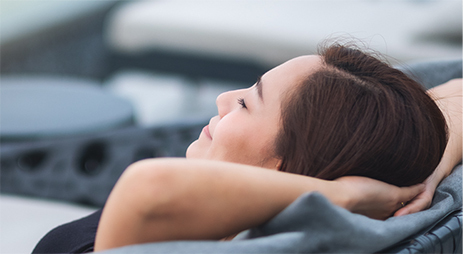 A woman leans back to relax with her arms tucked behind her head.