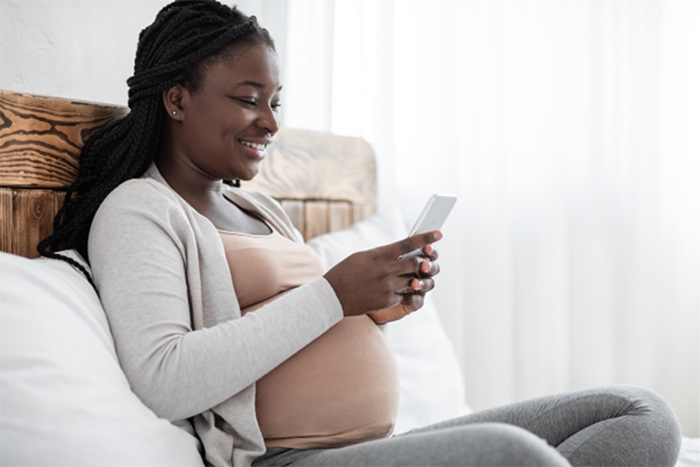 A pregnant woman relaxes in bed with her smartphone.