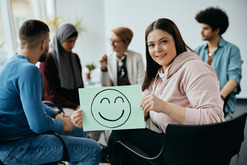 Woman holding smiley face sign in therapy meeting.