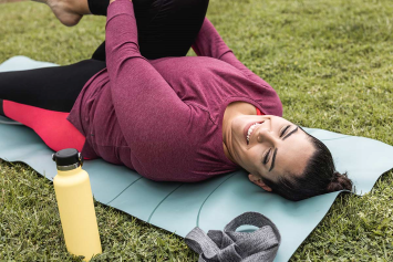 A person lays down outside on a yoga mat and stretches.
