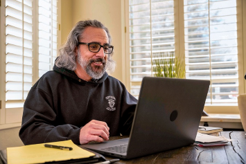 A person sitting at a table works on a laptop.
