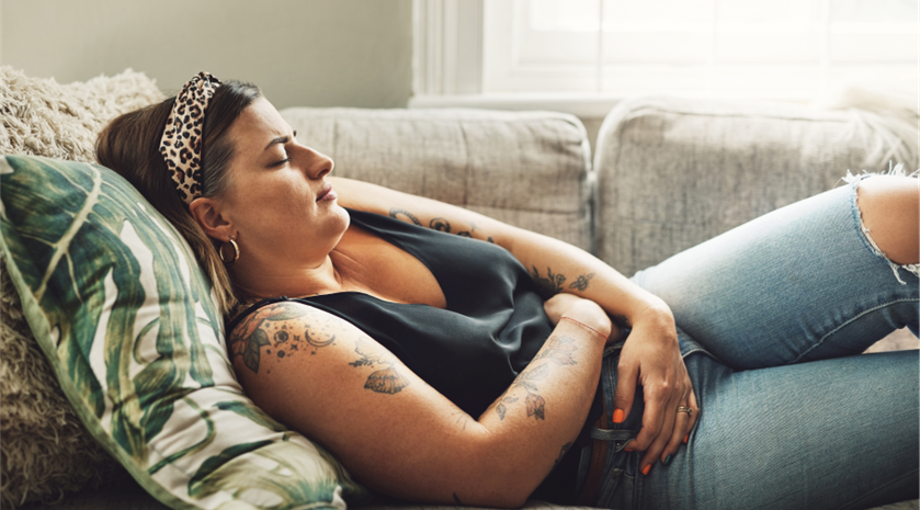 A woman leans back on a couch with her eyes closed.