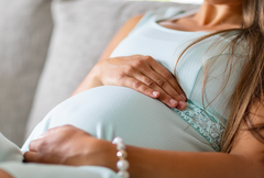 Pregnant woman laying on couch with hands on her belly.