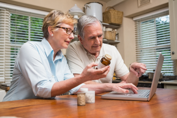 Two people look at a computer screen while examining a medicine bottle. 