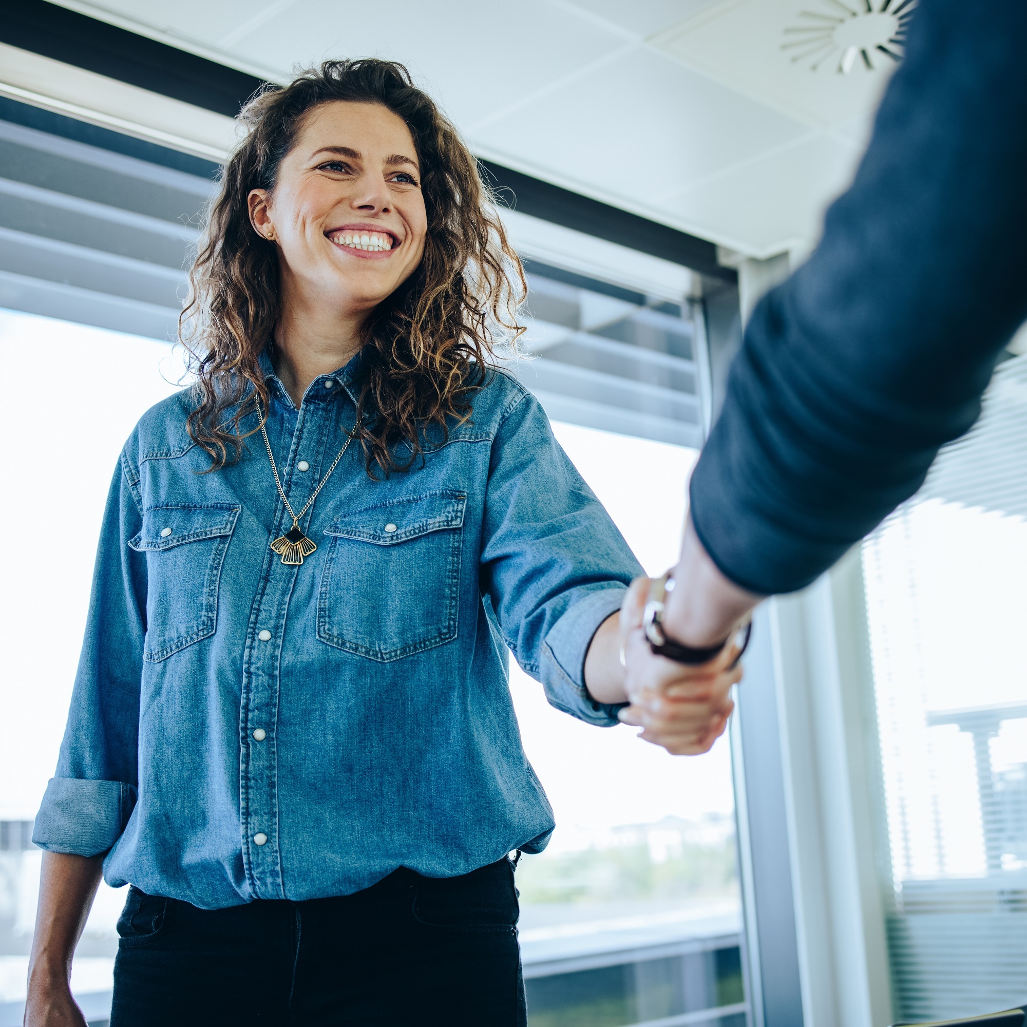 A professional setting where a woman shakes hands another person, illustrating a moment of partnership or business agreement